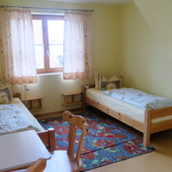 Kinderzimmer Ein Zimmer mit hellgelber Wandfarbe, zwei Betten an den Wänden und einem Kinderspielteppich in der Mitte.