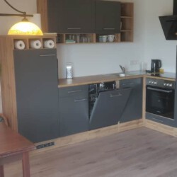 Ein Bild, das eine graue Küche und einen kleinen Esstisch aus Holz zeigt.